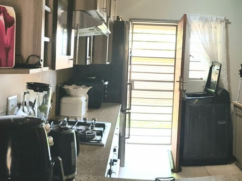 A functional kitchen featuring built-in cabinetry, stone countertops, a gas hob with extractor fan, and direct access to an exterior area via a security gate.