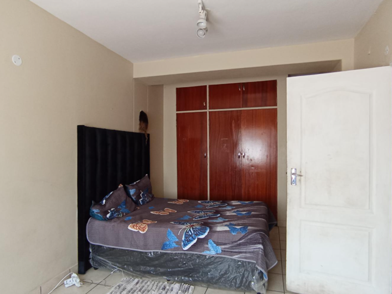 A bedroom featuring built-in wooden cupboards and tiled flooring, offering a functional space with potential for cosmetic updates.