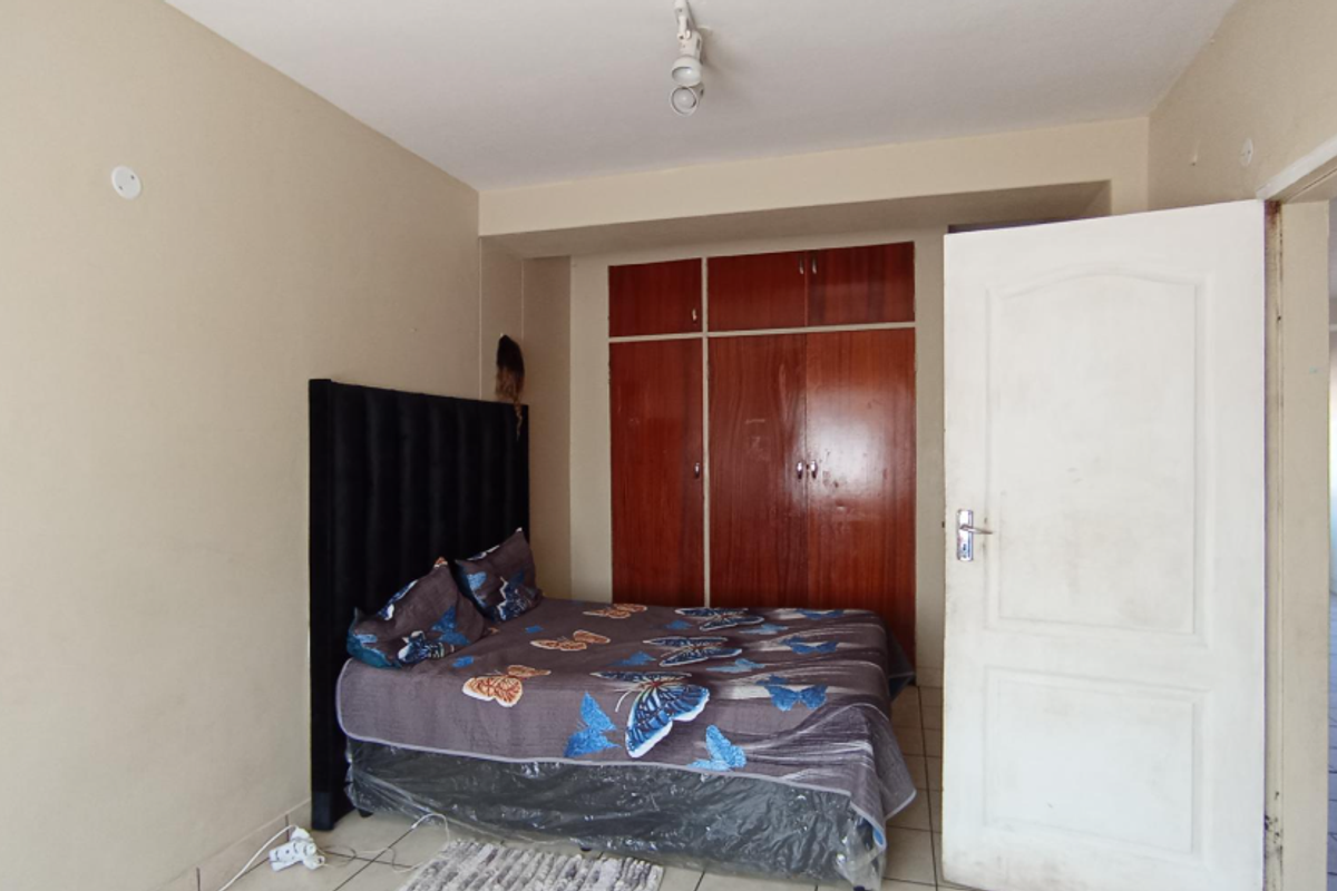 A bedroom featuring built-in wooden cupboards and tiled flooring, offering a functional space with potential for cosmetic updates.