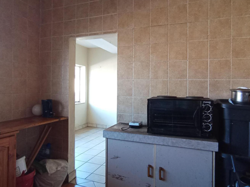 A dated kitchen area featuring tiled walls, built-in cabinetry, and a sink, with an adjacent room visible through the doorway.