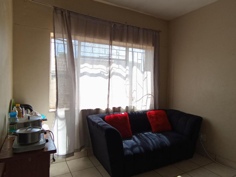A compact living area featuring tiled flooring and a window fitted with security bars, offering a functional space with potential for cosmetic updates.