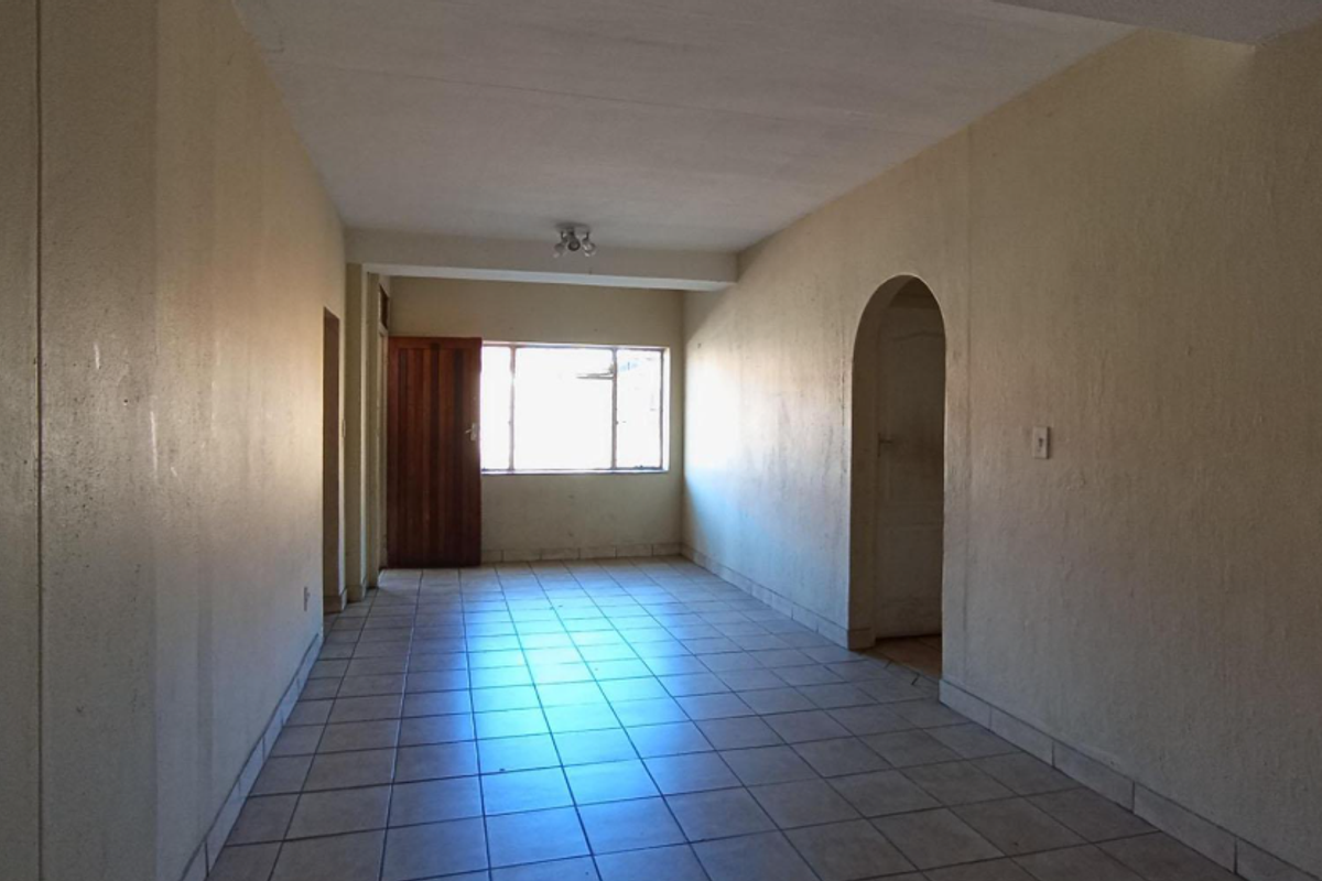 An empty, open-plan living area featuring tiled flooring, an arched doorway, and natural light from a rear window.