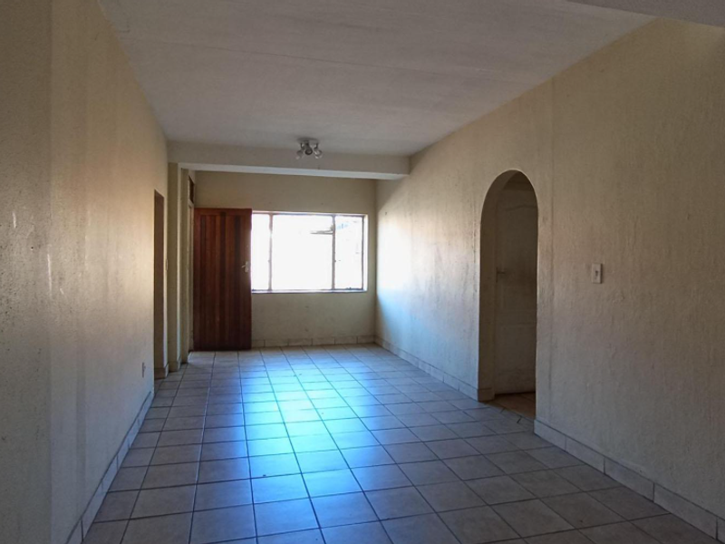 An empty, open-plan living area featuring tiled flooring, an arched doorway, and natural light from a rear window.