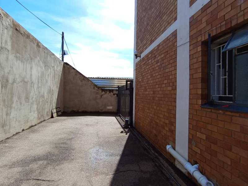 A narrow rear exterior area featuring brick building facade, perimeter wall, and paved ground surface with security gate access.