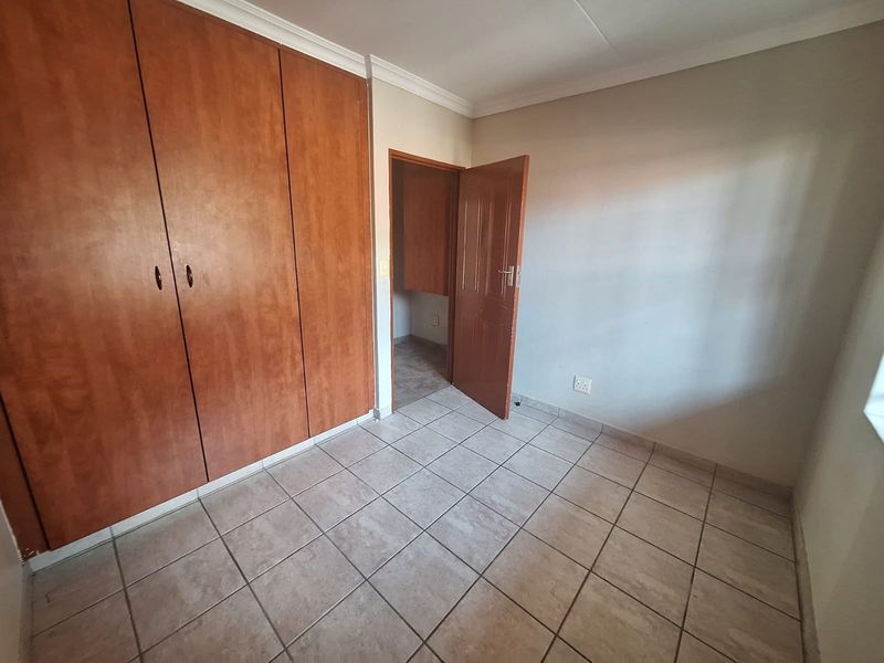 A clean, empty bedroom featuring tiled flooring, built-in wooden cupboards, and neutral wall finishes, offering a versatile space ready for personalization.