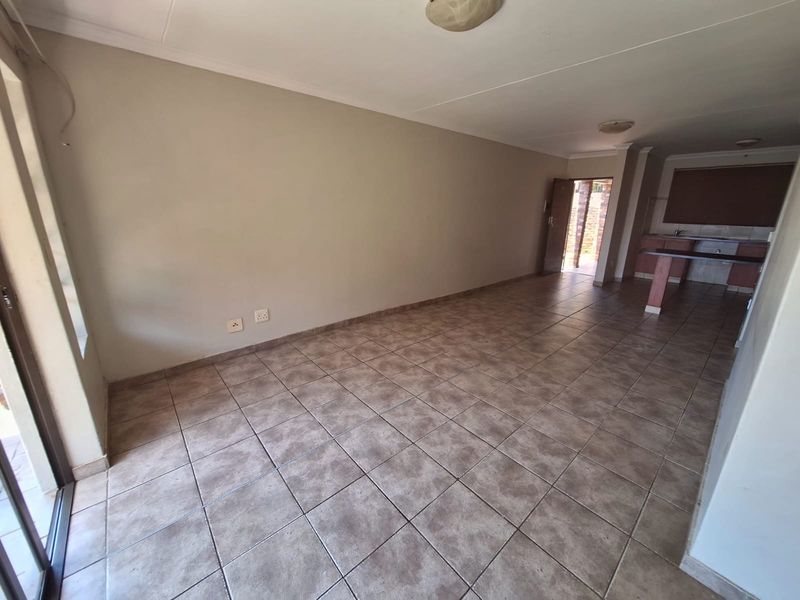 An open-plan living and kitchen area featuring tiled flooring, neutral walls, and direct access to an outdoor space through a sliding glass door.