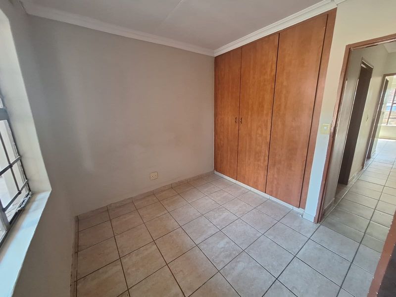 A vacant bedroom featuring tiled flooring, built-in wooden cupboards, and a window with security bars, offering a neutral canvas for personalization.