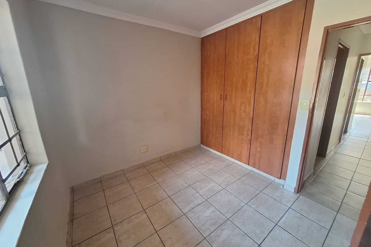 A vacant bedroom featuring tiled flooring, built-in wooden cupboards, and a window with security bars, offering a neutral canvas for personalization.