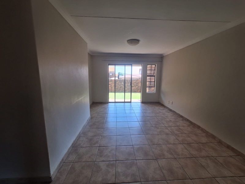 An empty, neutrally painted living room featuring tiled flooring, a ceiling cornice, and a sliding glass door providing access to the rear garden.