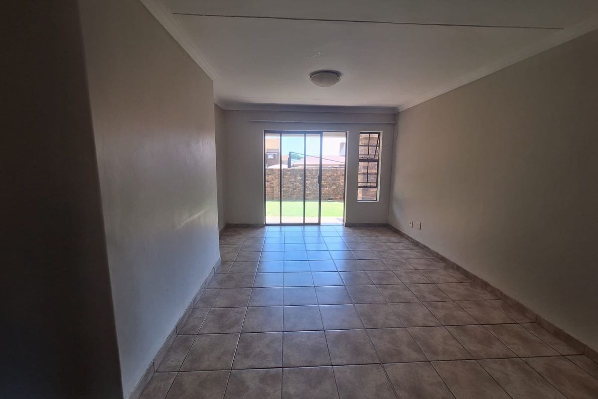 An empty, neutrally painted living room featuring tiled flooring, a ceiling cornice, and a sliding glass door providing access to the rear garden.