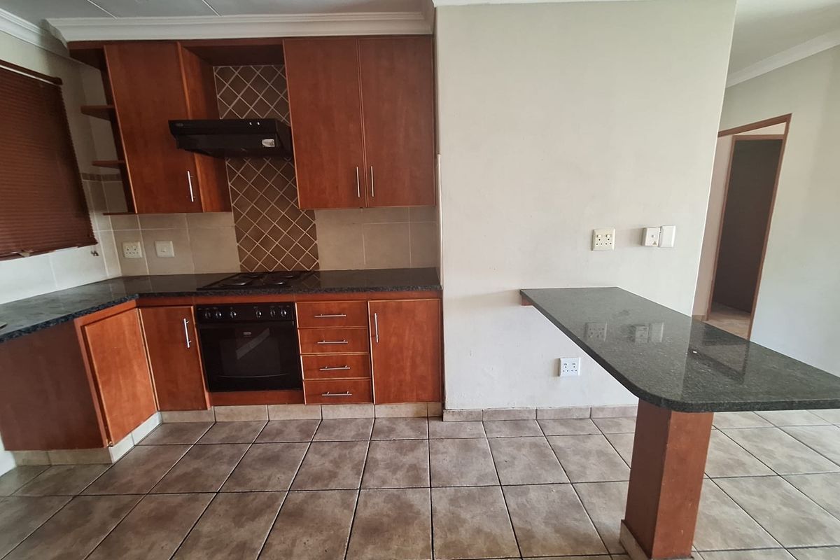 A functional kitchen featuring wooden cabinetry, granite countertops, a built-in oven with hob, and a breakfast bar, finished with tiled flooring and backsplash.