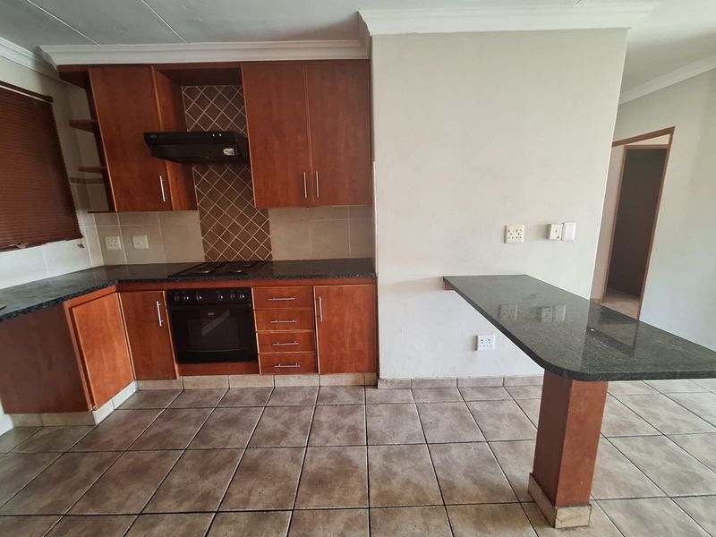 A functional kitchen featuring wooden cabinetry, granite countertops, a built-in oven with hob, and a breakfast bar, finished with tiled flooring and backsplash.