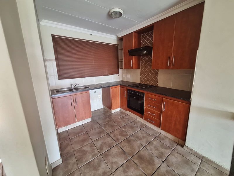 A functional kitchen featuring wooden cabinetry, built-in oven and hob, tiled flooring, and a double bowl sink with a tiled backsplash.