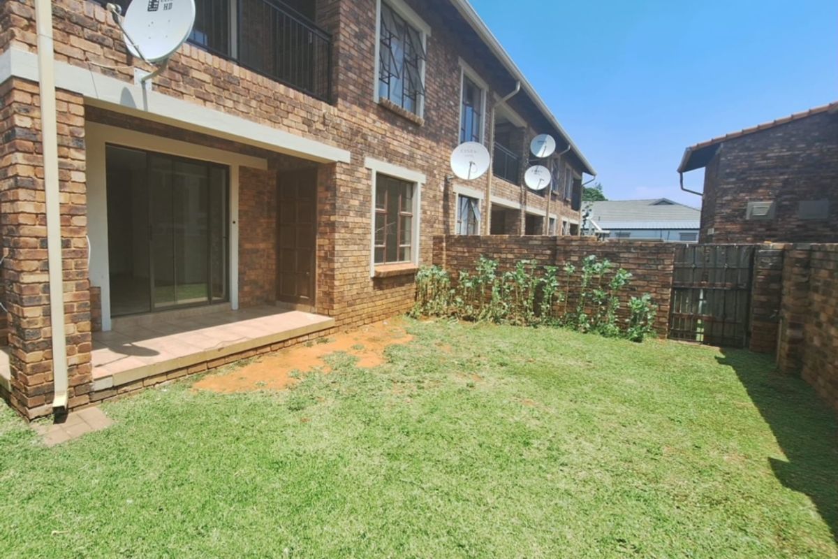 Rear view of a townhouse featuring a private garden, covered patio, and brick facade with security features and satellite dish installations.