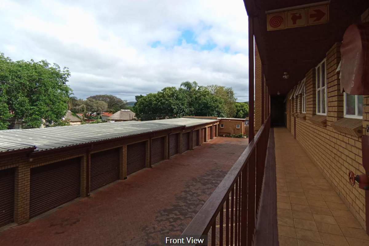 An elevated exterior view of the apartment complex walkway overlooking a row of brick garages with a paved driveway area.