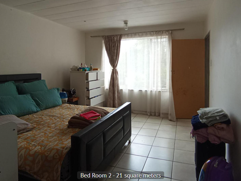 Spacious bedroom featuring tiled flooring, a large window with security bars, and neutral wall finishes.