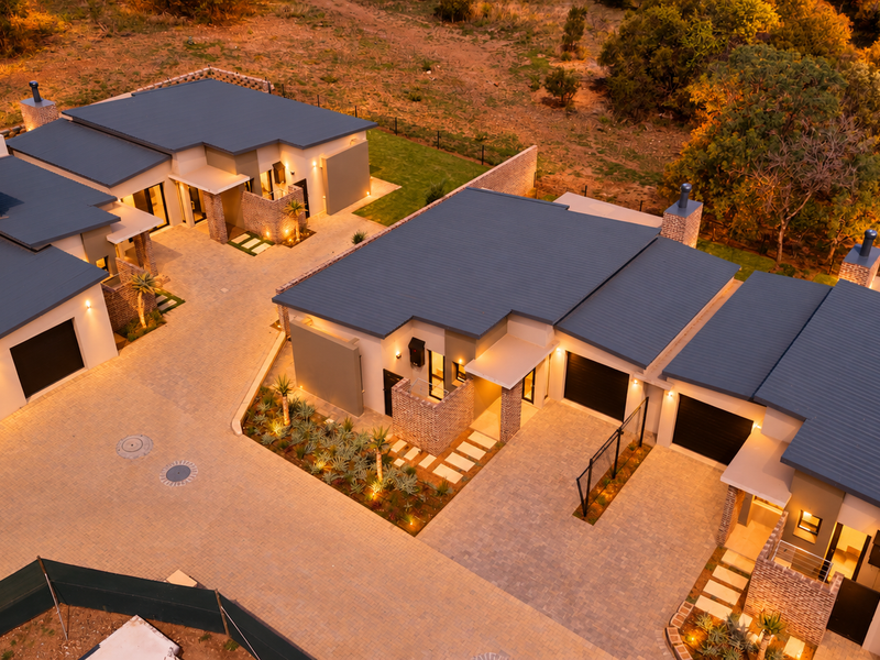 Aerial view of a modern retirement village complex featuring contemporary brick and metal roof architecture, paved driveways, and landscaped garden areas at dusk.