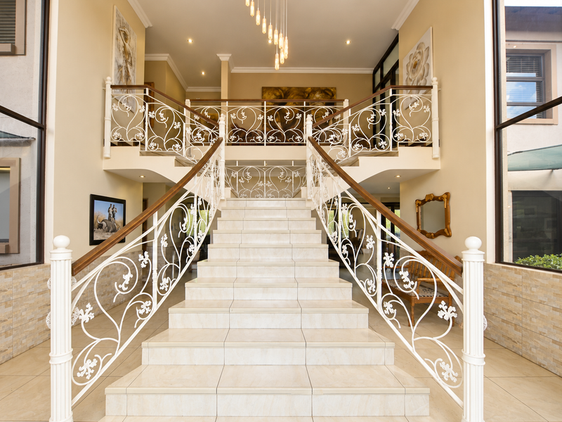 Grand entrance foyer featuring a central tiled staircase with ornate wrought iron balustrades, double-height windows, and elegant stone-clad wall accents.
