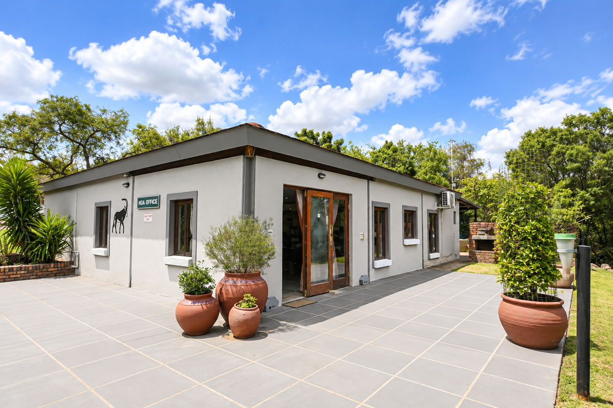 A well-maintained exterior rear view featuring a spacious tiled patio, built-in brick braai area, and direct access to the building through glass double doors.