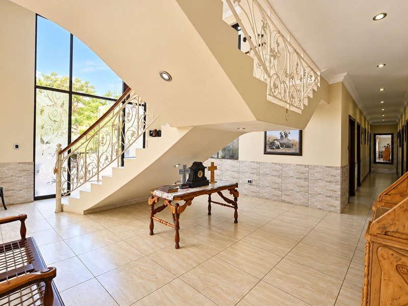 Spacious entrance hall featuring a grand staircase with decorative wrought iron railings, large windows, and neutral tiled flooring throughout.