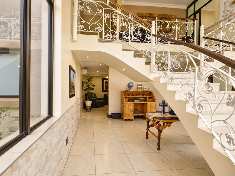 Spacious entrance hallway featuring a grand staircase with ornate wrought iron balustrades, tiled flooring, and a large window providing natural light.