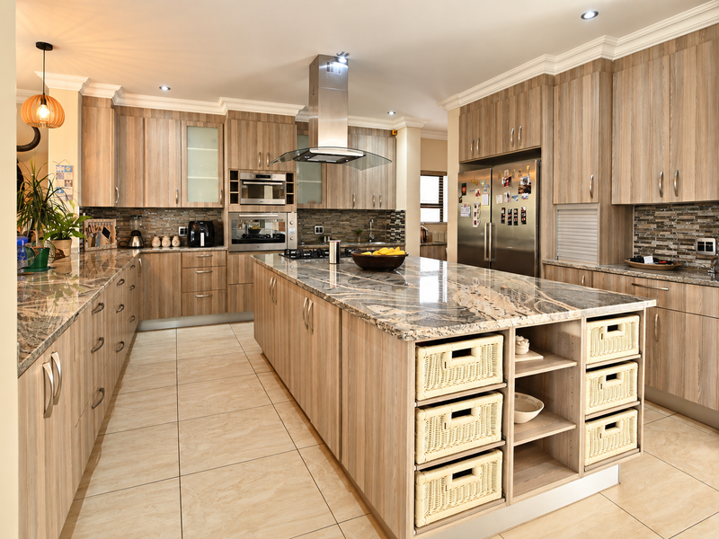 Spacious modern kitchen featuring wood-look cabinetry, granite countertops, a large central island, and high-end built-in appliances with a mosaic tile backsplash.