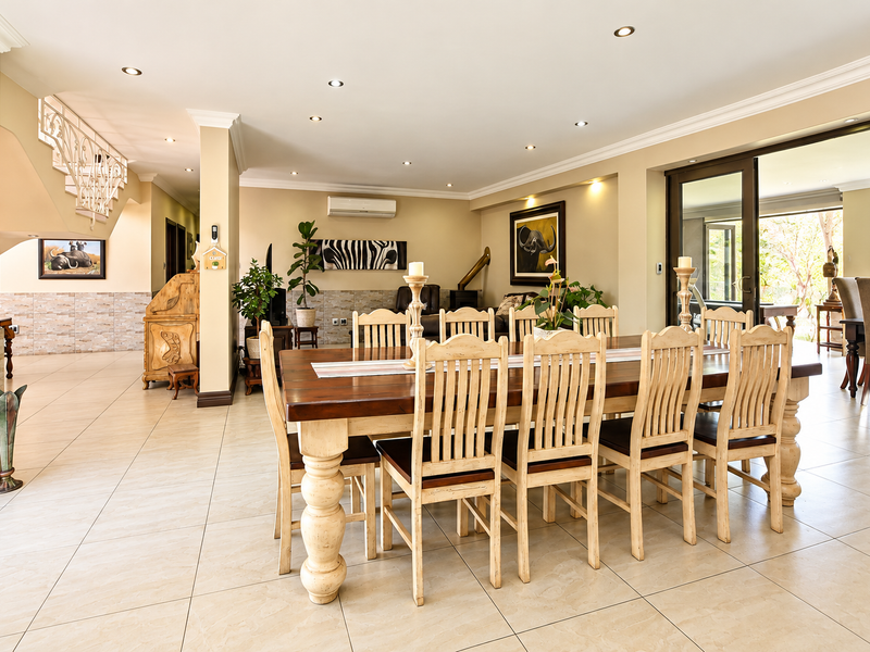 Spacious open-plan dining and living area featuring tiled floors, recessed lighting, a feature stone wall, and direct access to the outdoor patio through sliding doors.