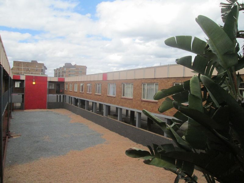 View of the apartment complex rear courtyard featuring a brick facade, concrete support pillars, and a gravel ground surface.