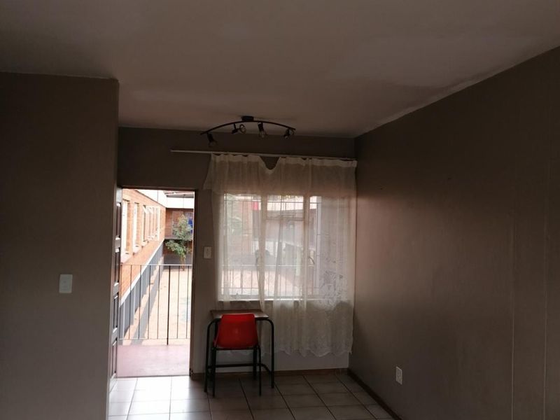 A sparsely furnished living area featuring tiled flooring, ceiling track lighting, and direct access to an external walkway.