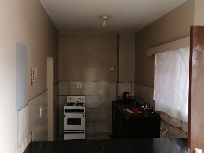A small, dated kitchen area featuring a freestanding stove, basic cabinetry, and tiled splashbacks, currently requiring significant cosmetic repairs and finishing to the wall surfaces.