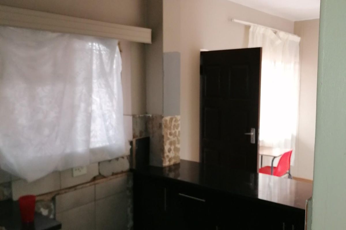 A kitchen area featuring dark built-in cabinetry and stone countertops, currently requiring repairs to the wall tiling and finishes.