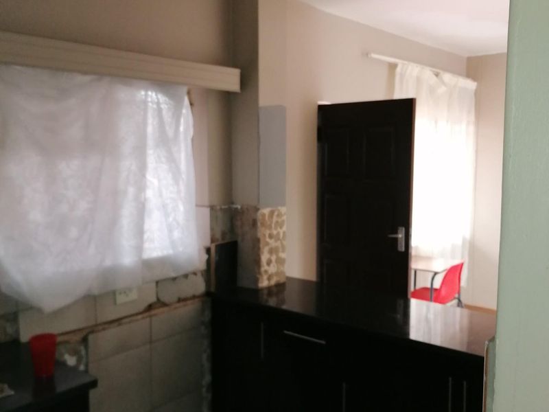 A kitchen area featuring dark built-in cabinetry and stone countertops, currently requiring repairs to the wall tiling and finishes.