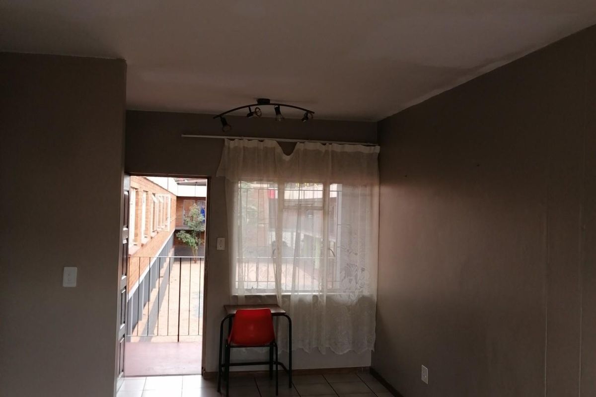 An empty living area featuring tiled flooring, a ceiling spotlight fixture, and direct access to an exterior balcony through a security gate.