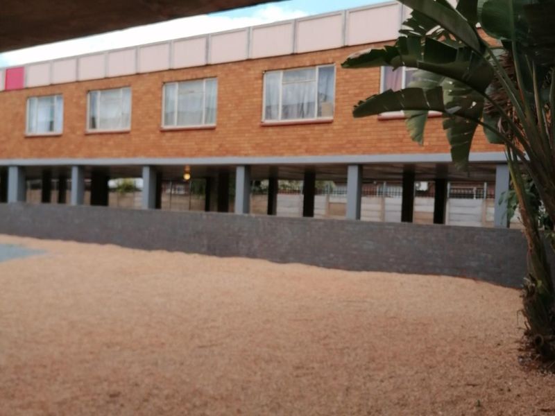 A view of the rear exterior of the apartment building, featuring a brick facade, elevated structure, and a gravel courtyard area.