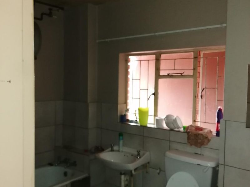 A dated bathroom featuring a standard bathtub, pedestal basin, and toilet, with security bars on the window and tiled splashback areas.