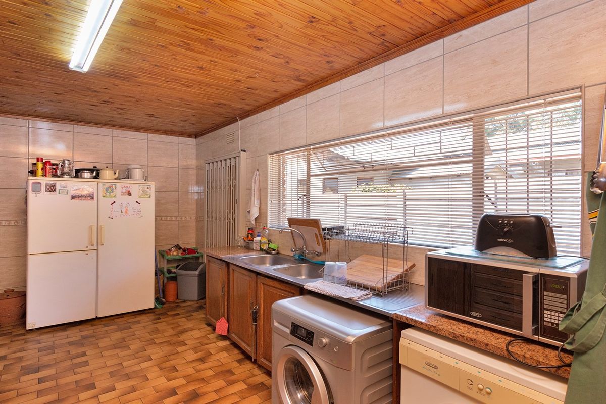 A functional kitchen featuring tiled walls, timber ceiling, double sink, and built-in cabinetry with space for laundry appliances.
