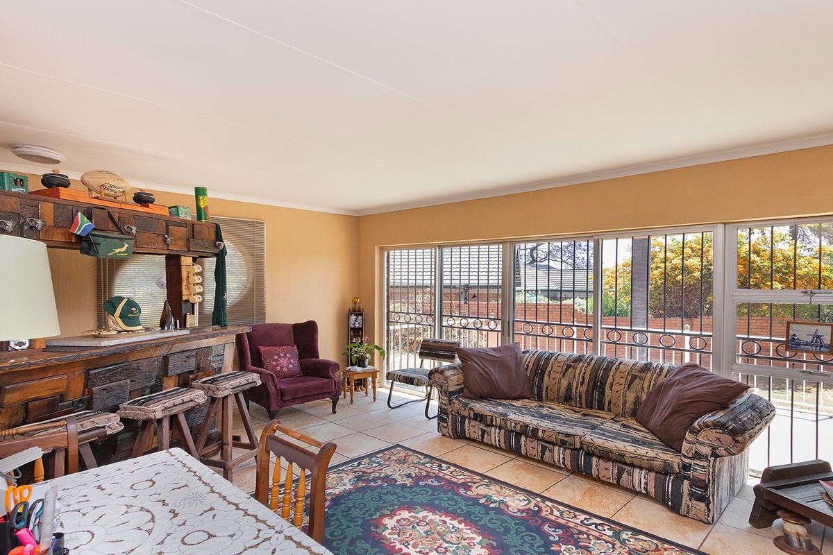 Spacious living area featuring a built-in wooden bar, tiled flooring, and large sliding glass doors with security bars leading to the exterior.