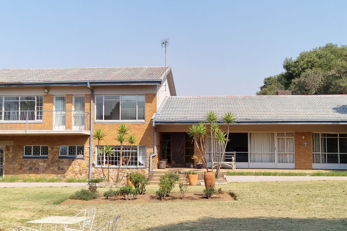 Rear view of a two-story farm-style residence featuring a combination of brick and stone cladding, a tiled roof, and a spacious garden area.