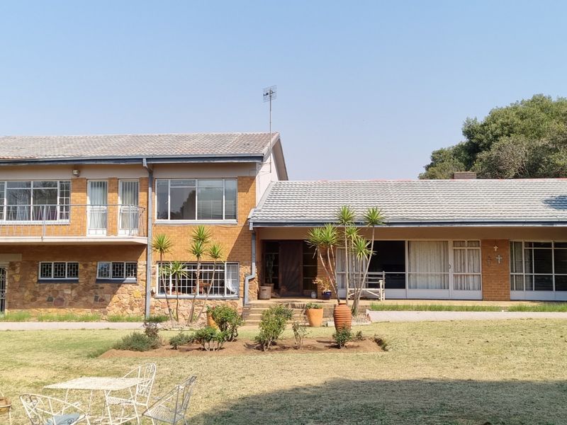 Rear view of a two-story farm-style residence featuring a combination of brick and stone cladding, a tiled roof, and a spacious garden area.