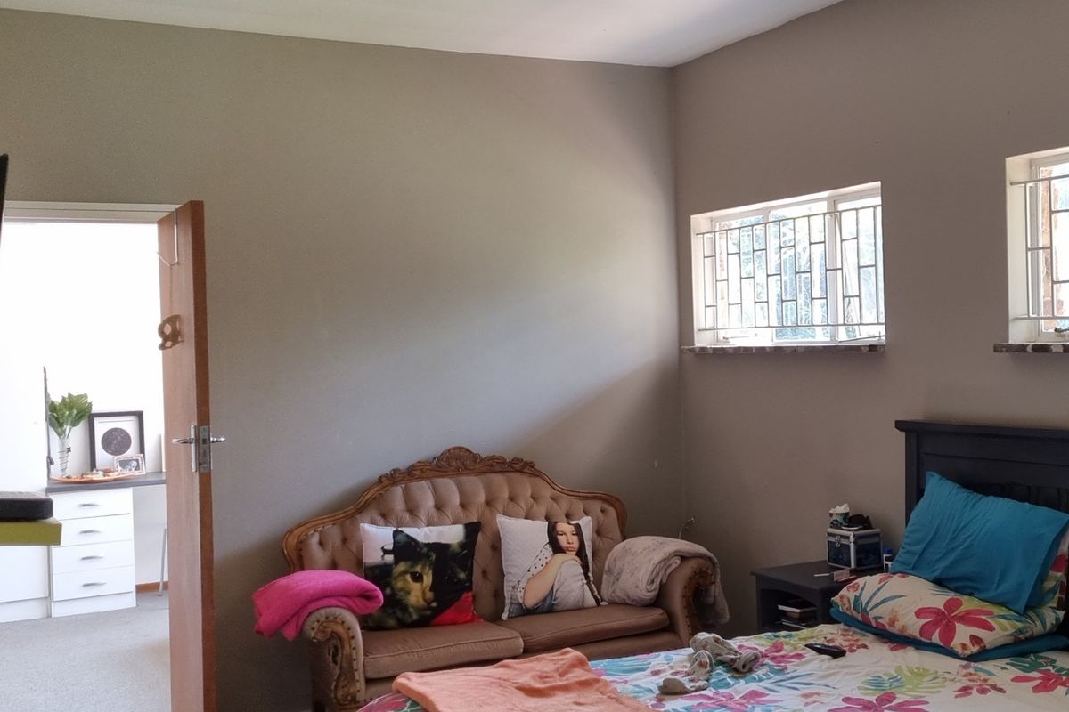 A bedroom featuring neutral wall tones, security bars on the windows, and an adjoining room visible through the open doorway.