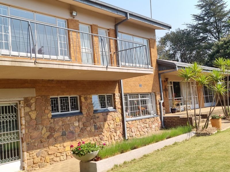 Rear view of a two-story brick and stone farmhouse featuring a balcony with metal railings, security bars on windows, and a paved patio area.