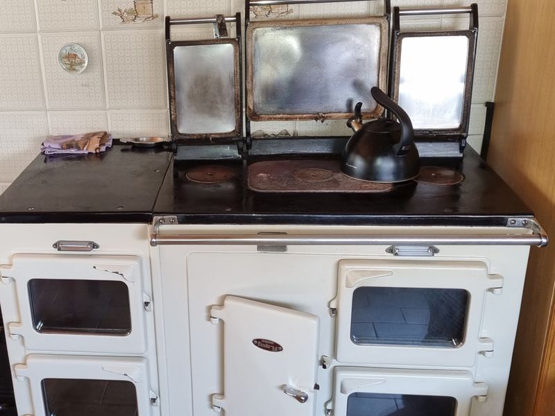A vintage-style built-in range cooker with multiple oven compartments and a tiled splashback, showing signs of age and wear.
