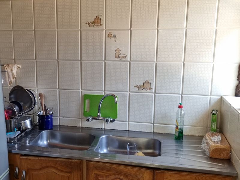A functional kitchen area featuring a stainless steel double sink, wall-mounted tap, and decorative ceramic wall tiling above wooden base cabinetry.