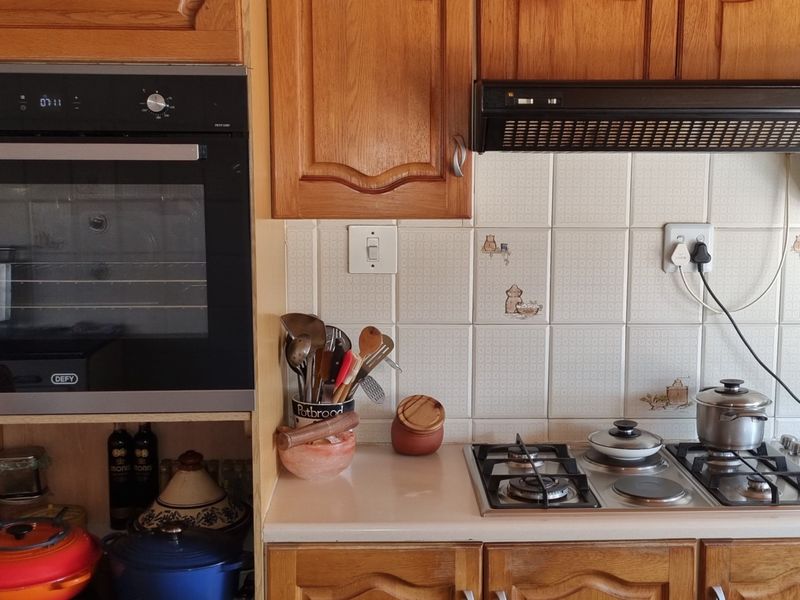 A functional kitchen area featuring wooden cabinetry, a built-in Defy oven, and a combination gas and electric hob with a tiled backsplash.
