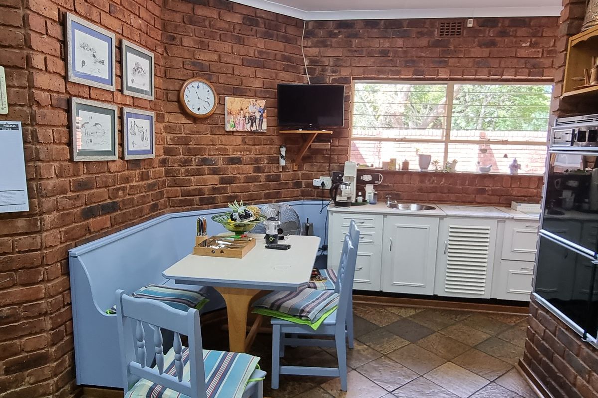 A kitchen area featuring exposed brick walls, white cabinetry, a built-in oven, and tiled flooring with an integrated dining nook.