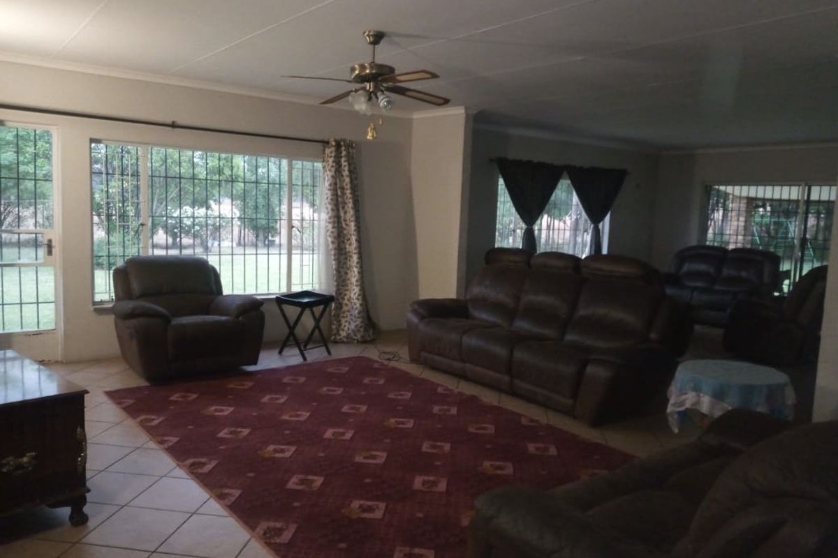 Spacious living room featuring tiled flooring, a ceiling fan, and large windows with security bars, offering views of the surrounding garden.
