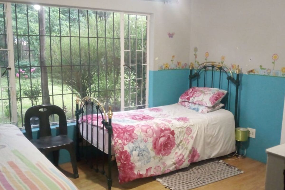 A bedroom featuring laminate flooring and large windows with security bars, overlooking the garden area.