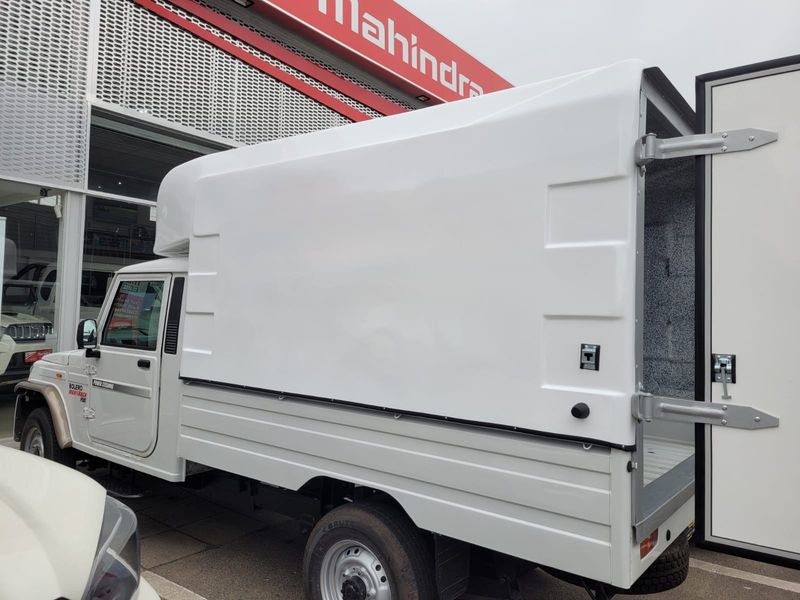 A white Mahindra Bolero pickup truck with a custom cargo canopy parked at a dealership.