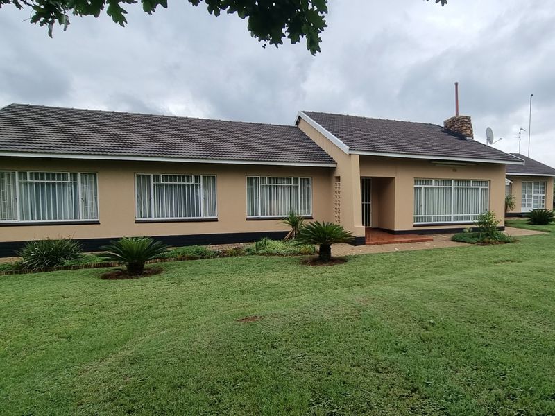 Front elevation of a well-maintained single-story home featuring a tiled roof, brick chimney, and security bars on windows, set within a spacious garden.
