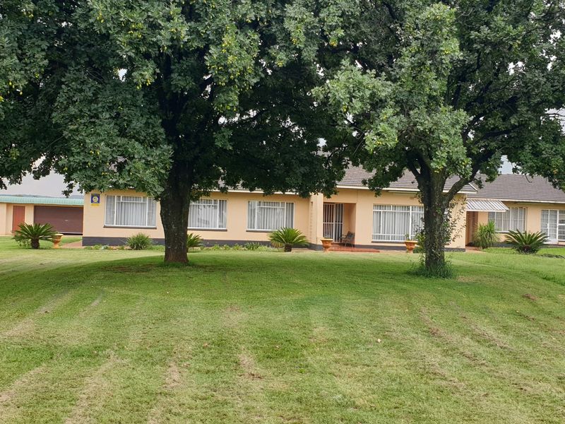 Front view of a single-story residence featuring a tiled roof, large mature trees, and a well-maintained lawn.